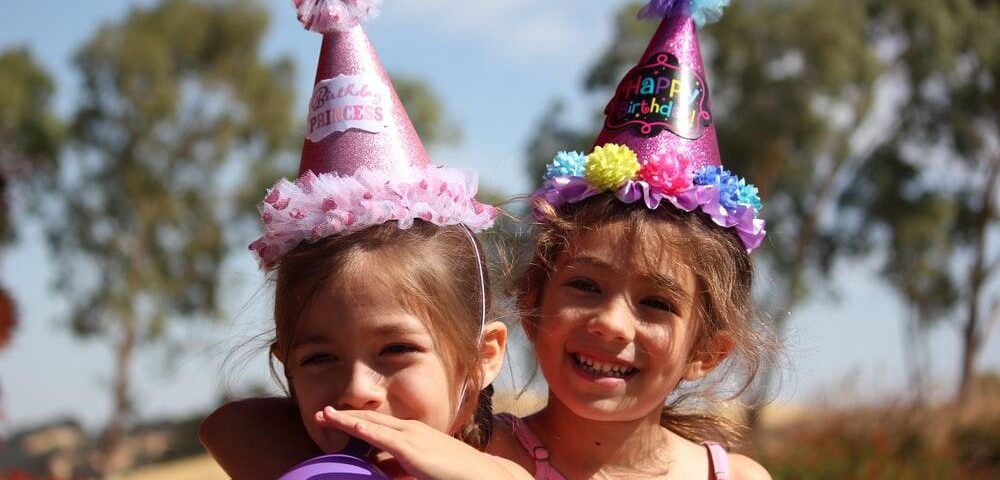 Two cute little girls wearing birthday hats at a birthday party
