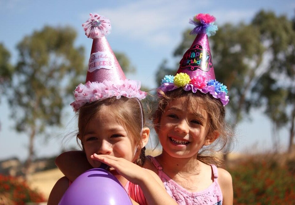 Two cute little girls wearing birthday hats at a birthday party