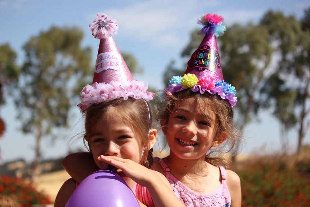 Two cute little girls wearing birthday hats at a birthday party
