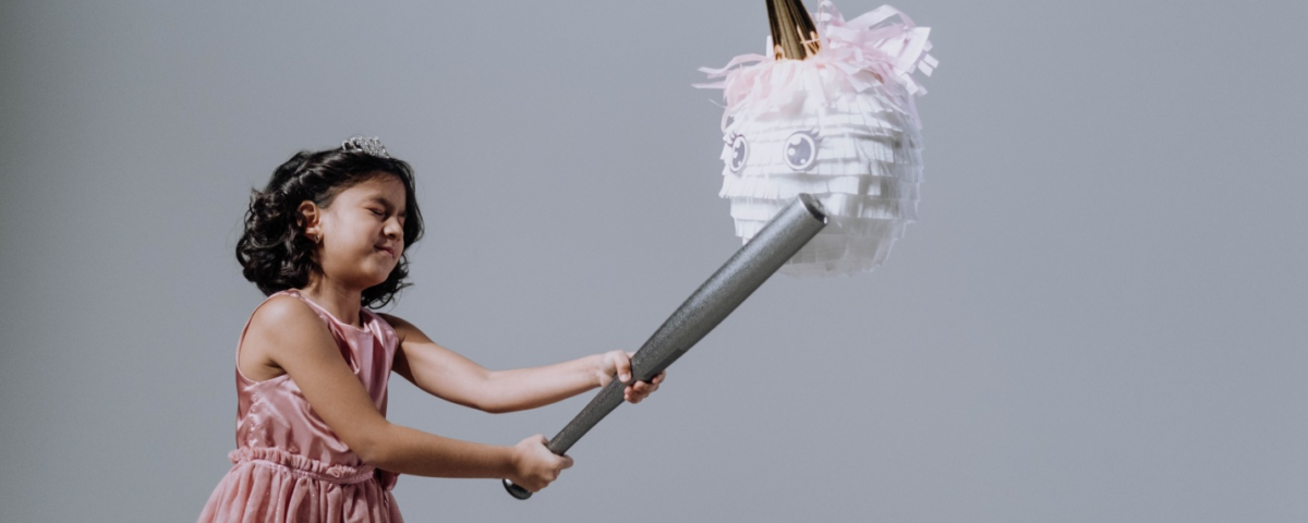 A girl in a pink dress hitting a piñata with a baseball bat