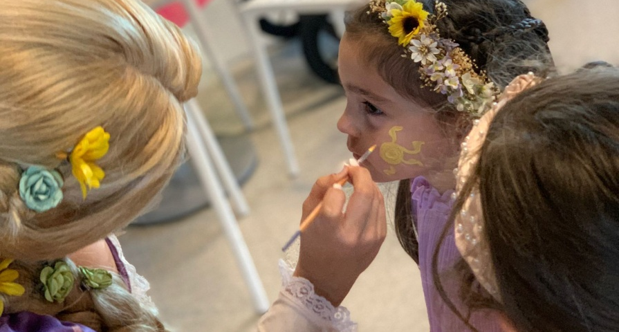 A dressed-up woman face painting a child