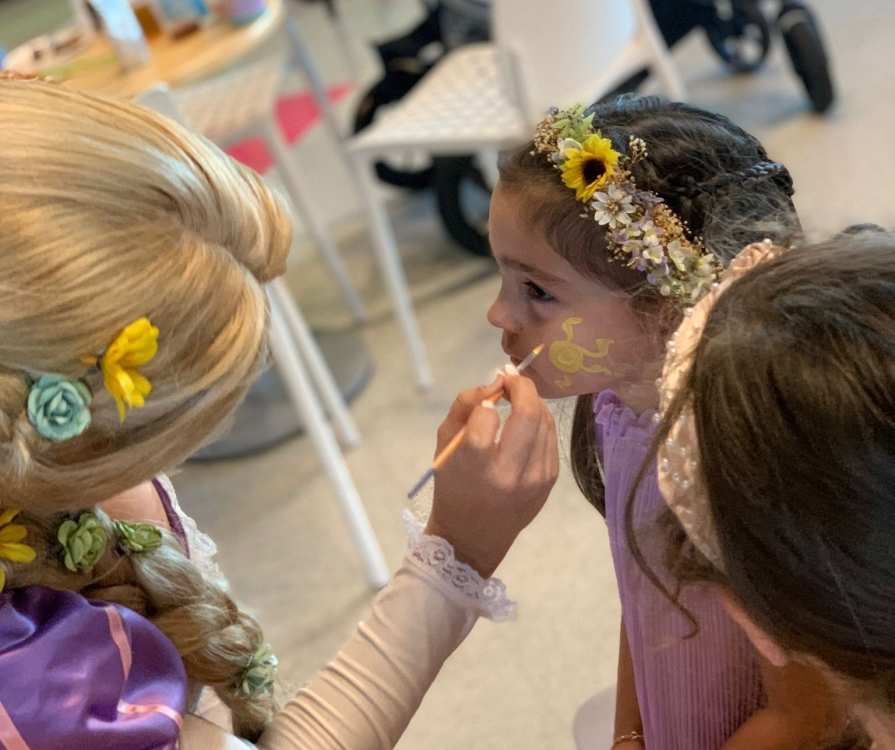 A dressed-up woman face painting a child